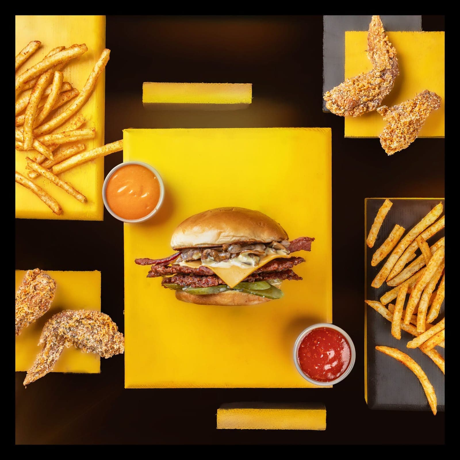 Top-down spread of a burger, fries and wings on yellow boards